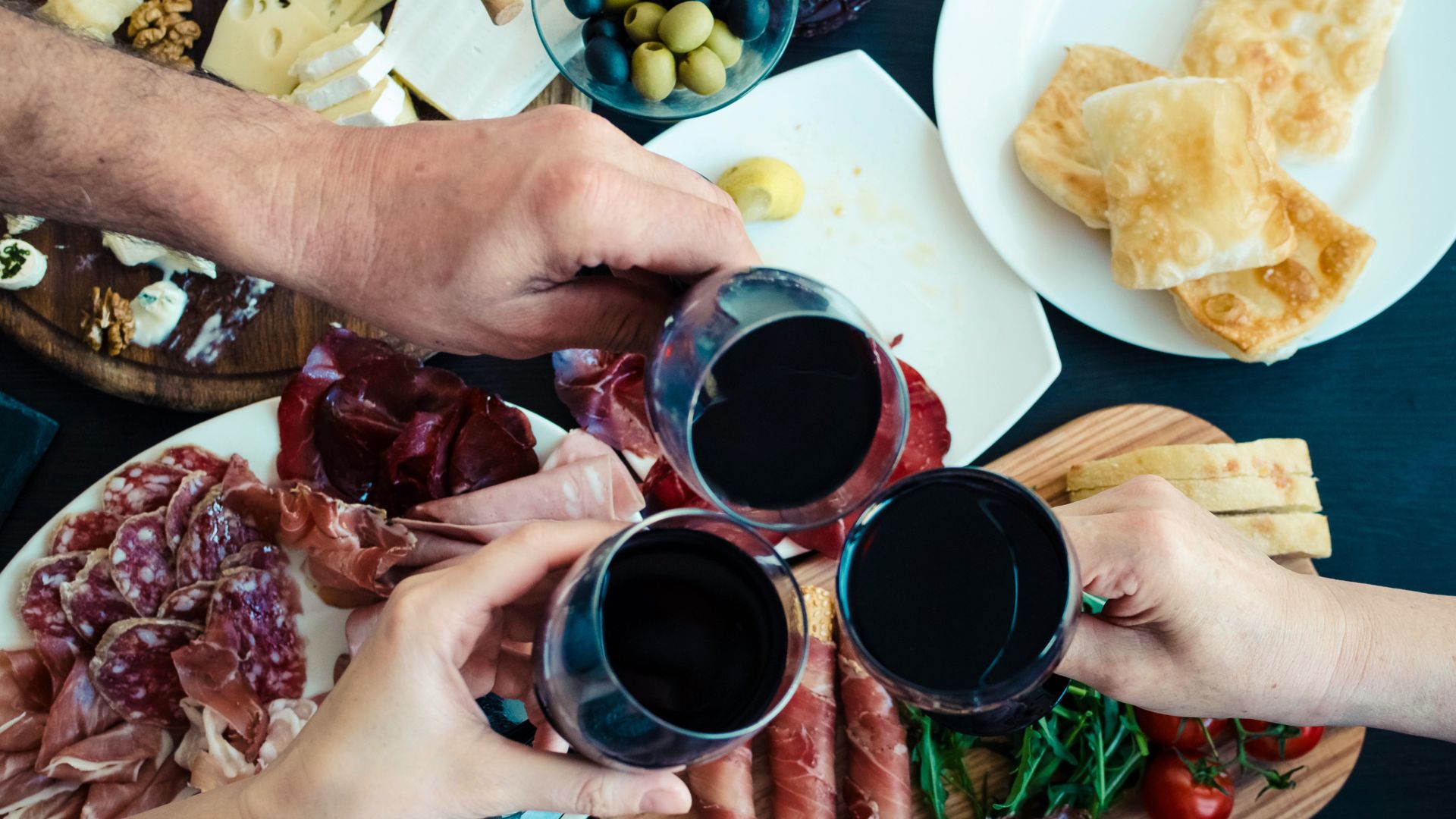 Three wine glasses clanking over charcuterie board